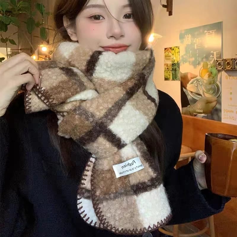 Young woman wearing a large plaid fuzzy beige and brown checked winter scarf with embroidered edges indoors