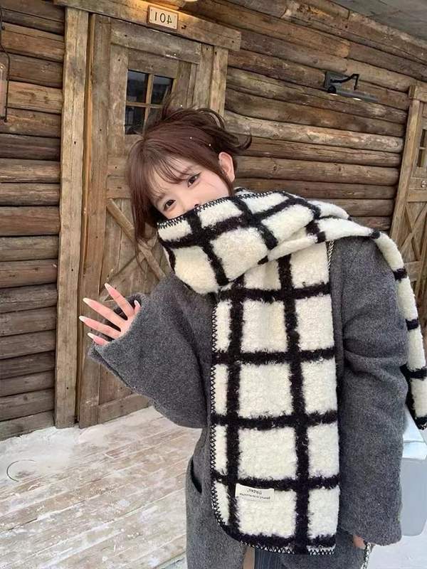 Woman wearing oversized black and white plaid fluffy wool scarf over gray coat near rustic wooden cabin in winter