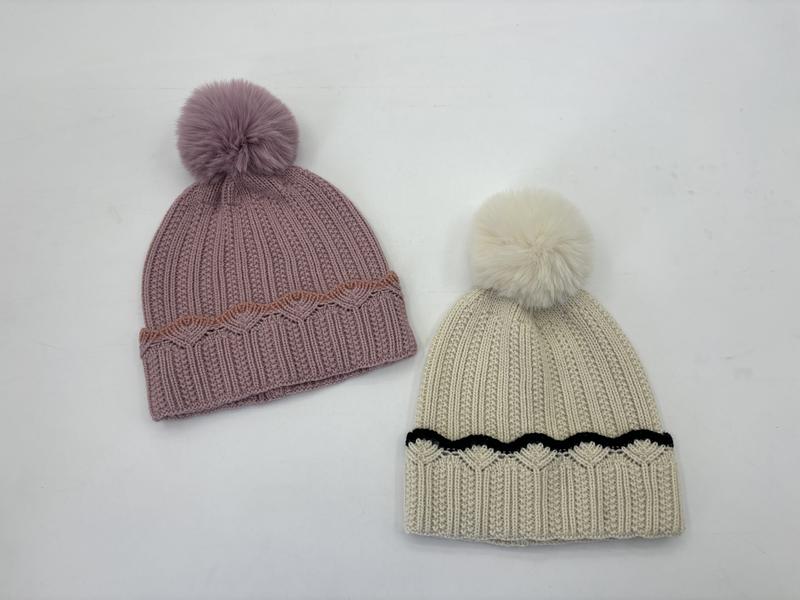Two ribbed knit pom-pom beanies laid flat: dusty pink with rust scallop trim and cream with black scallop trim, each with faux fur pompom
