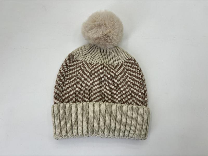 Cream knit beanie hat with brown chevron zigzag pattern and fluffy faux fur pom pom on white background