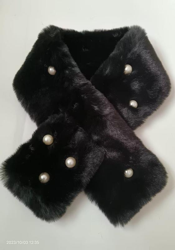 Black faux fur crossover neck scarf with decorative white pearl buttons laid flat on white background
