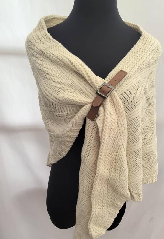 Cream chunky cable knit wrap shawl with brown leather buckle fastener displayed on black mannequin, cozy winter accessory