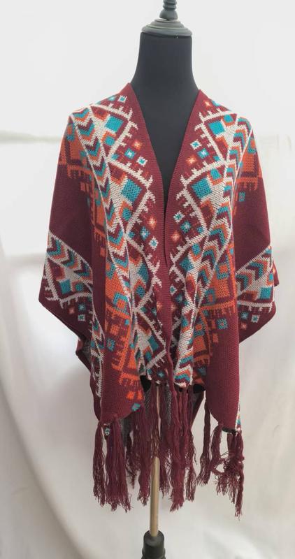 Burgundy knit poncho with multicolor Aztec geometric pattern in teal orange and white displayed on dress form with tassel fringe hem