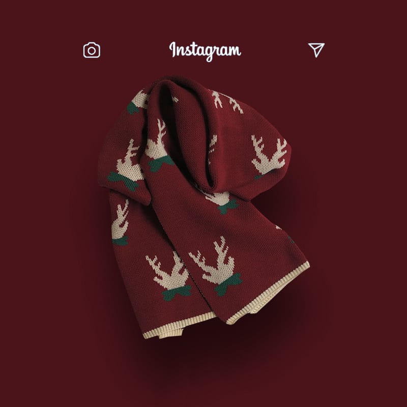 Burgundy knitted scarf with repeating reindeer pattern in cream and green, folded on dark red background
