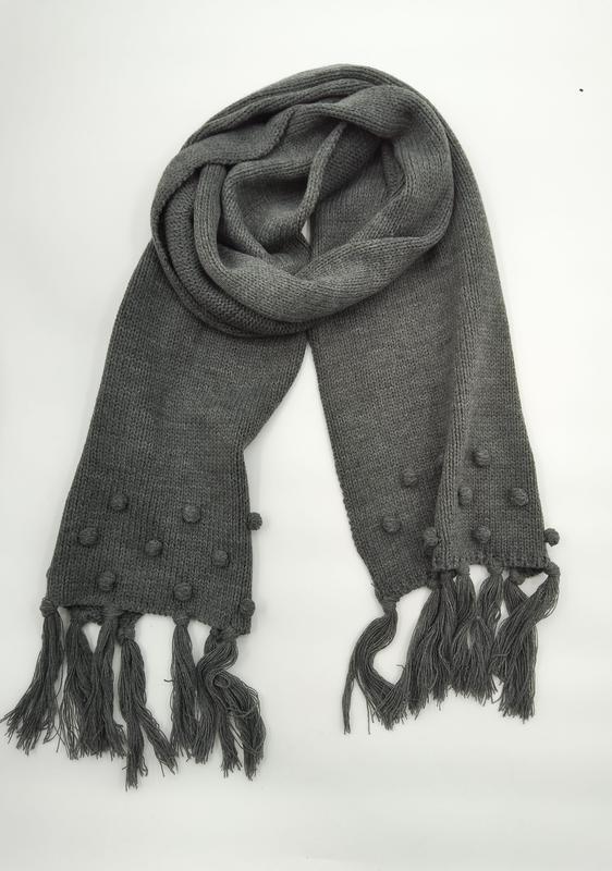 Gray chunky knit scarf with bobble texture detailing and long tassel fringe ends, coiled on white background