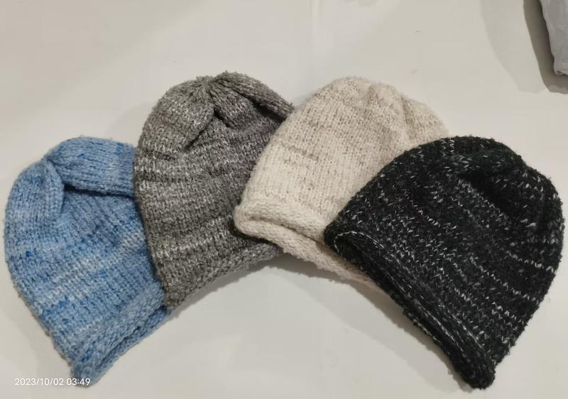 Four hand-knitted wool beanie hats in blue, gray, cream, and black laid flat on white surface