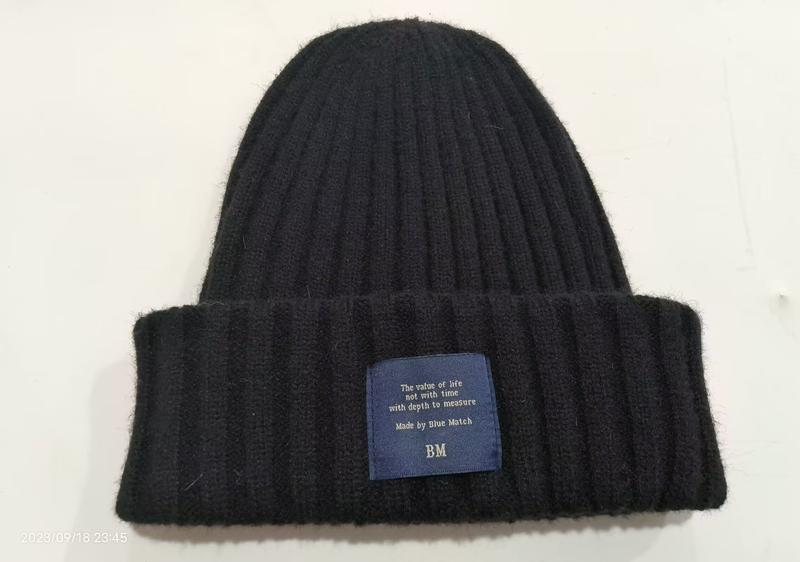Black chunky ribbed knit winter beanie hat with folded cuff and blue brand label on white background