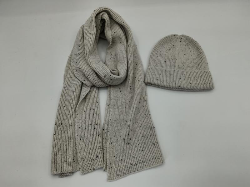 Light gray ribbed knit scarf and matching beanie hat with dark speckle pattern laid flat on white background