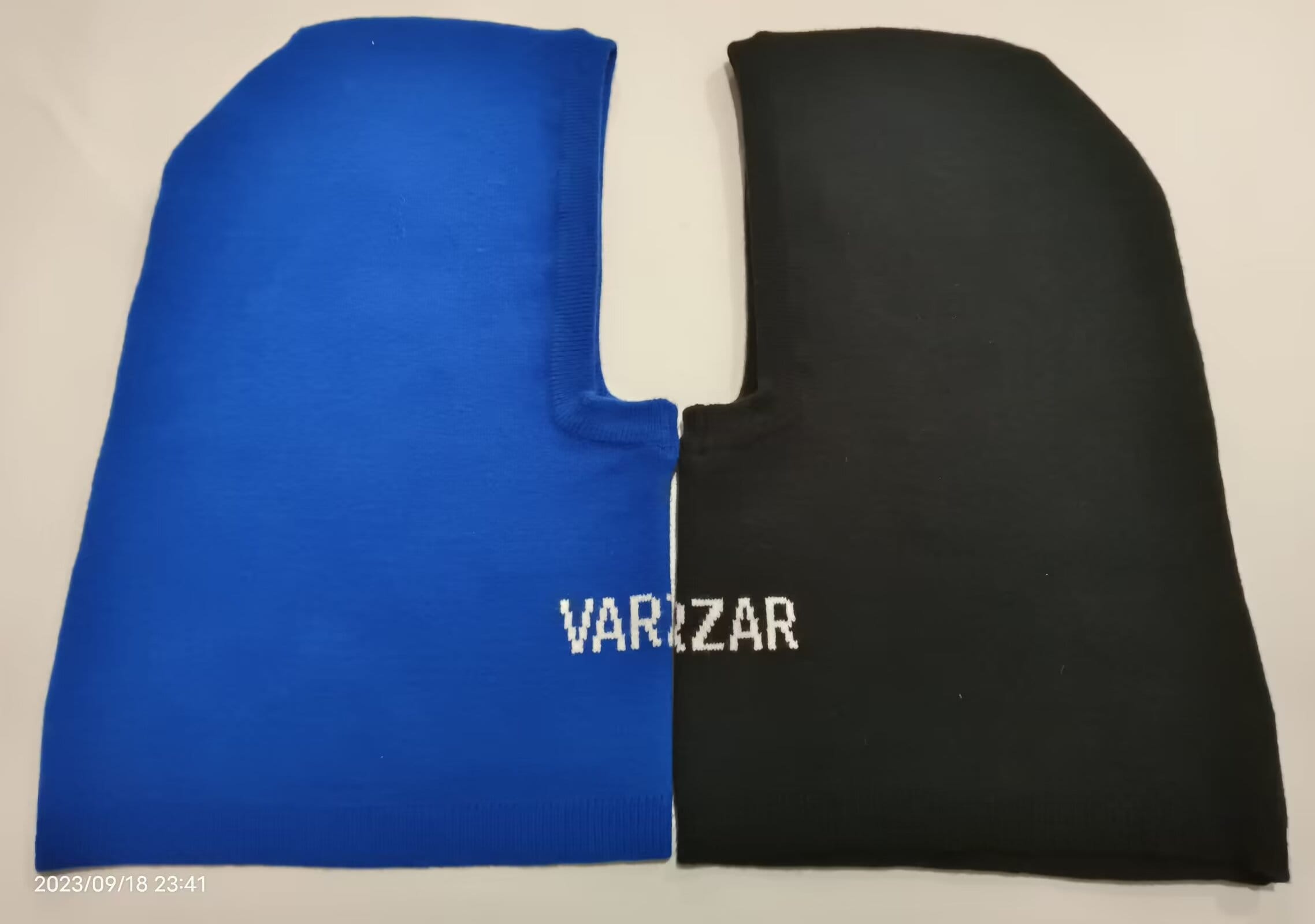 Blue and black two-tone knit balaclava laid flat showing face opening and brand logo on black side