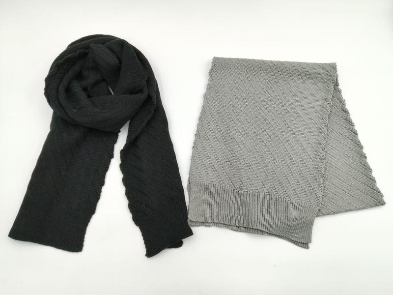 Two knit scarves flat lay: black draped scarf and folded light grey herringbone pattern scarf with ribbed edges on white background
