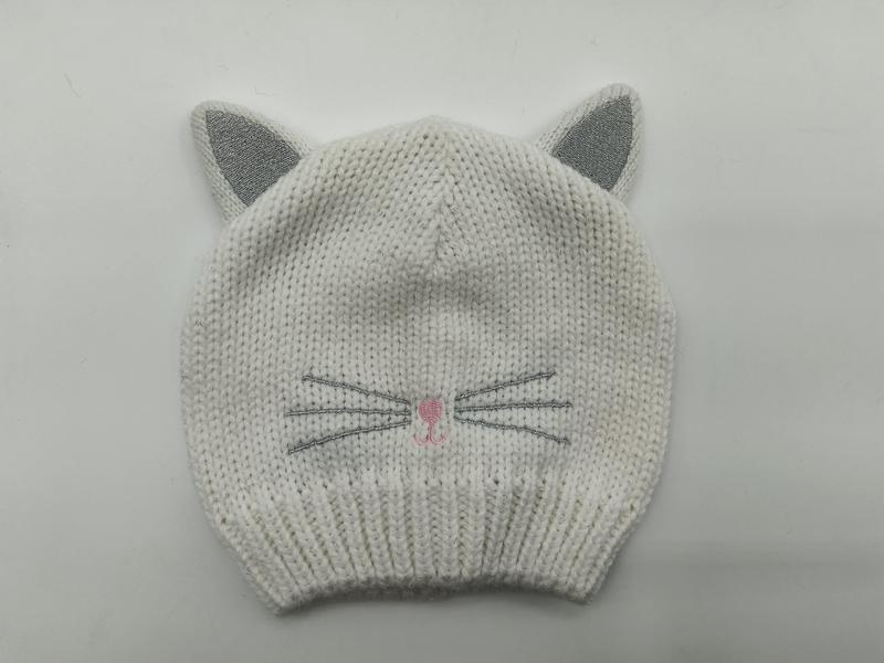 White chunky knit baby beanie hat with silver glitter cat ears, embroidered whiskers and pink nose detail on gray background