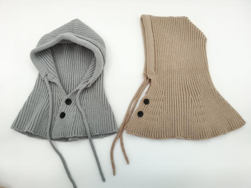 Two ribbed knit hooded neck warmers in gray and beige with black buttons and drawstring ties, laid flat on white background