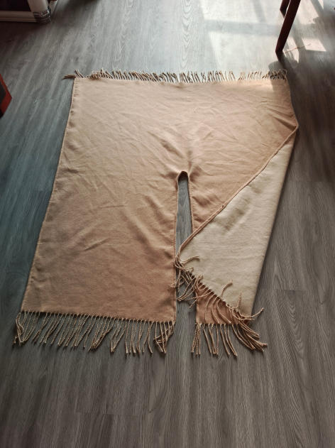 Reversible beige and cream woven throw blanket with twisted rope fringe trim laid flat on hardwood floor