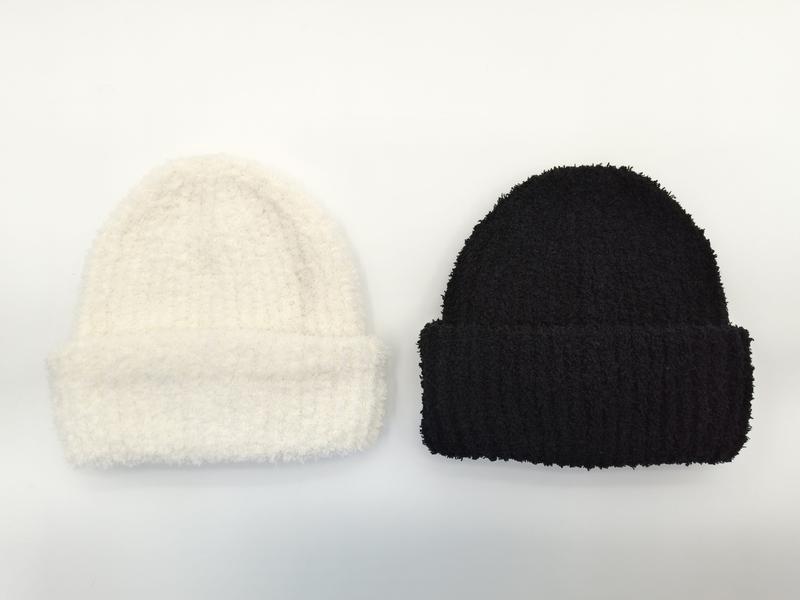 Two fuzzy ribbed knit beanies laid flat on white background, one cream and one black, with folded cuffs