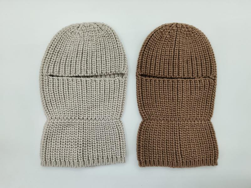 Two chunky knit balaclava ski masks laid flat, one in light beige and one in warm brown, showing eye slit opening and ribbed texture