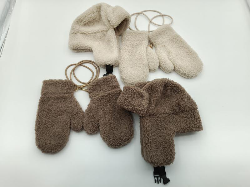 Two sherpa fleece trapper hat and mitten sets in cream and brown, connected by elastic cords, laid flat on white surface