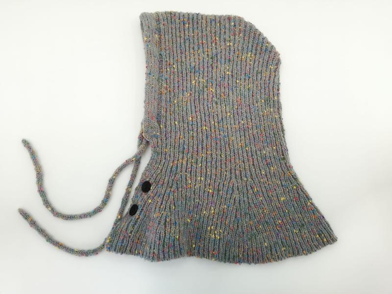 Flat lay of a gray multicolor speckled knit baby bonnet with chin ties and two black snap buttons on white background