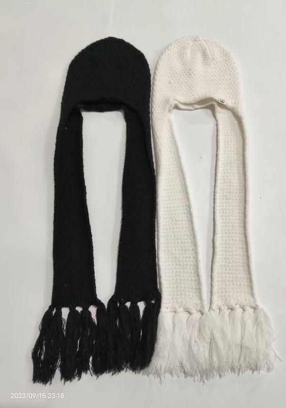Two knitted hooded scarf hats with long tasseled ends laid flat, one black and one white, earflap balaclava winter style