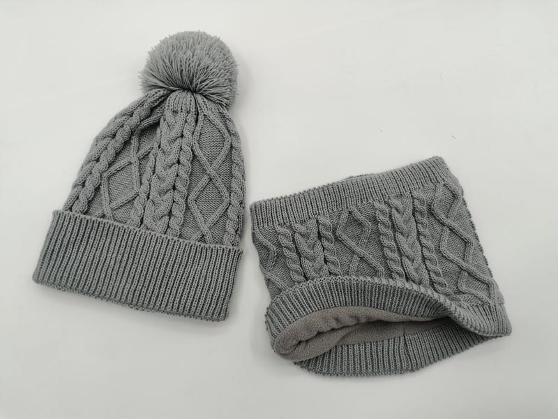 Grey cable knit winter beanie hat with pom pom and matching fleece-lined neck gaiter set on white background
