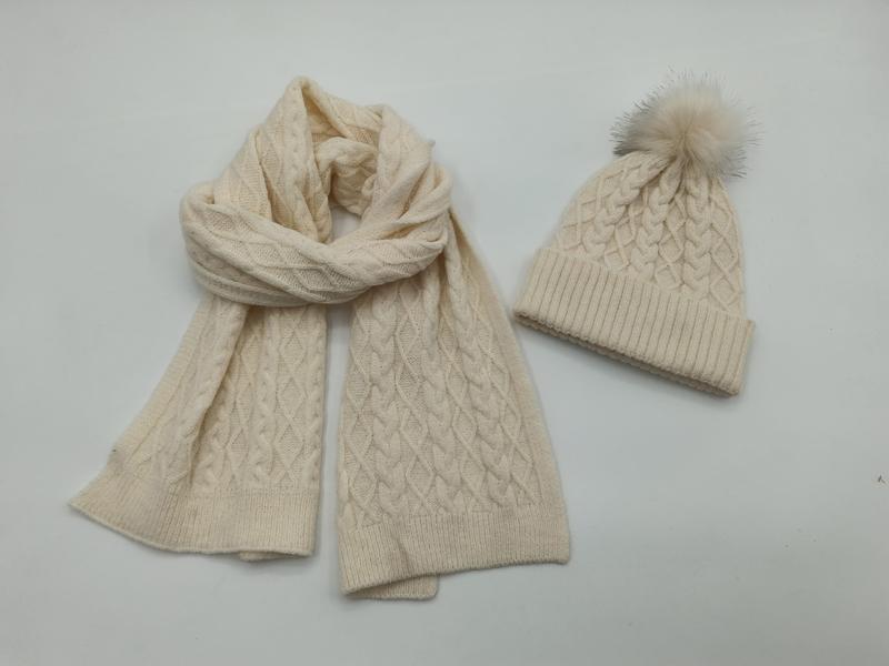 Cream cable knit winter scarf and matching beanie hat with faux fur pom-pom on white background