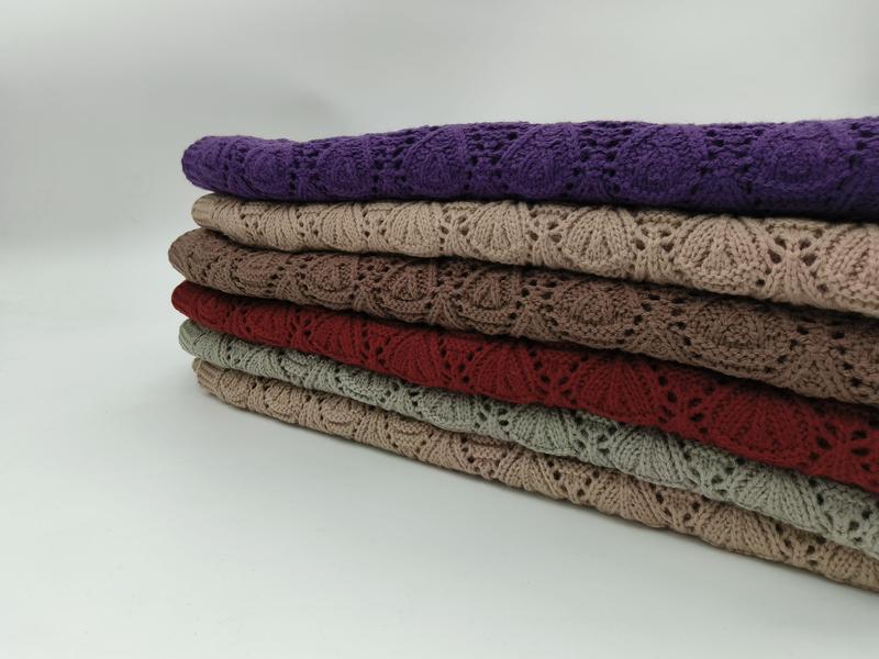 Stack of six folded lace knit throw blankets in purple, beige, taupe, red, sage green, and tan with floral openwork pattern
