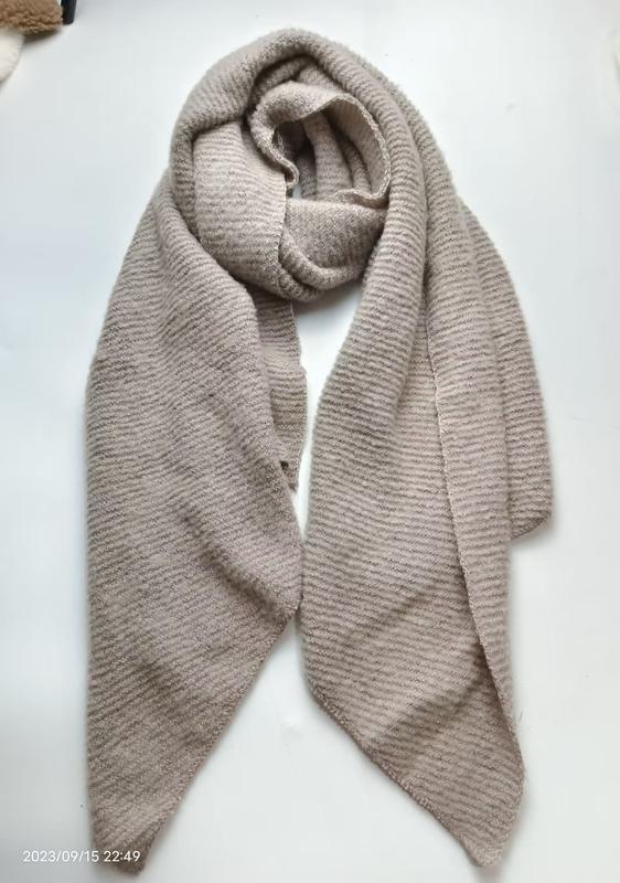 Beige ribbed knit scarf loosely wrapped and laid flat on white surface, showing soft textured stripe pattern