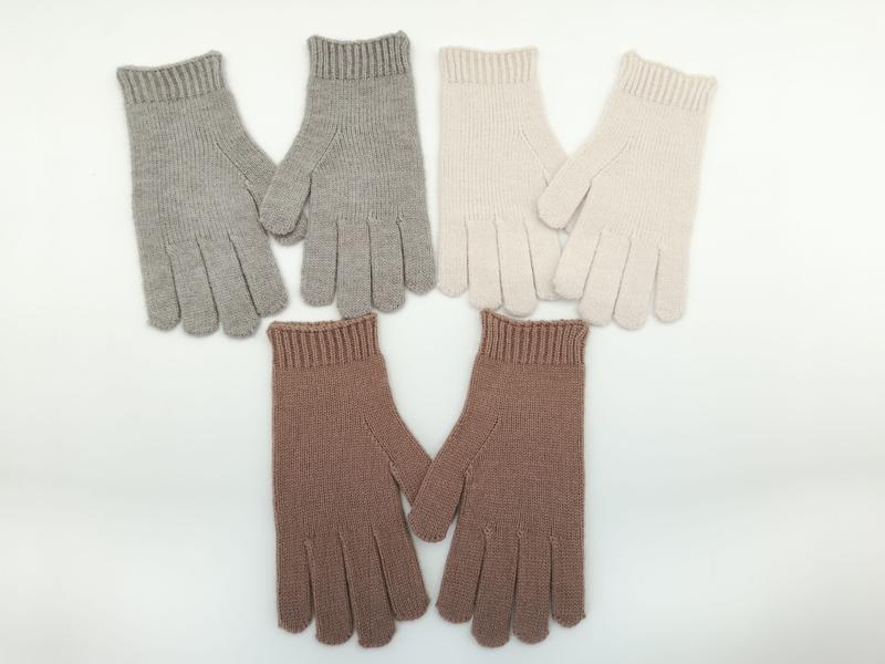Three pairs of ribbed knit winter gloves in light grey, cream, and mauve pink laid flat on white background