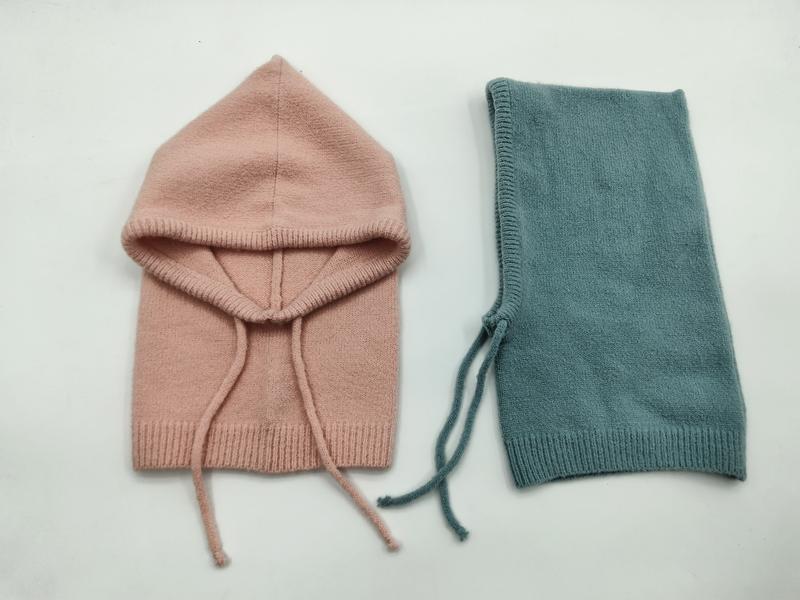 Two knit baby balaclavas laid flat, one blush pink with hood open and one folded teal, both with drawstring ties