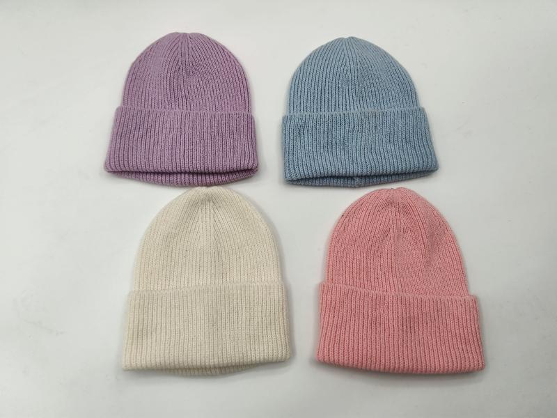Four ribbed knit cuffed beanie hats in pastel lavender, blue, cream, and pink laid flat on white surface