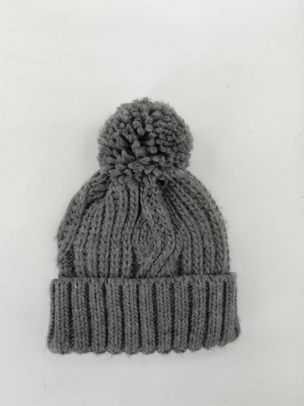 Grey chunky cable knit winter beanie hat with large pom pom and ribbed cuff, flat lay on white background