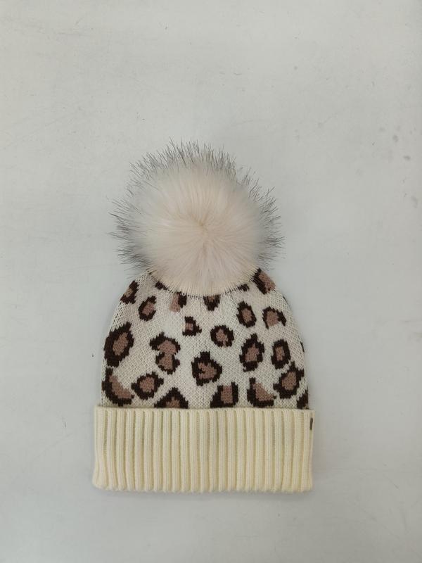 Cream knit beanie with brown leopard print pattern and fluffy white faux fur pom-pom on top, ribbed cuff