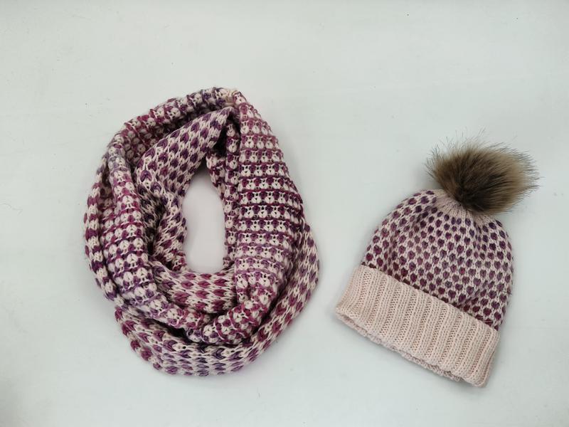 Matching knit winter set with purple and cream infinity scarf and beanie hat with faux fur pom-pom on white background