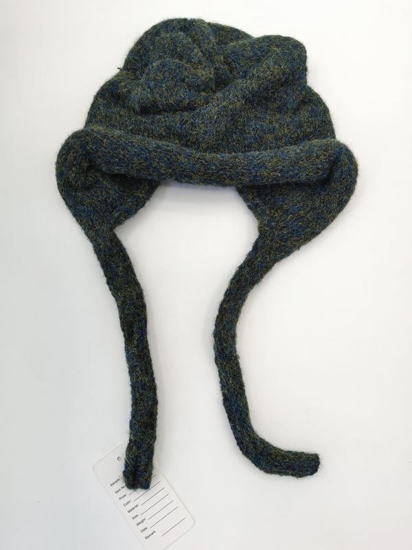 Chunky knit blue-green marl wool earflap winter hat with long braided ties laid flat on white background with product tag