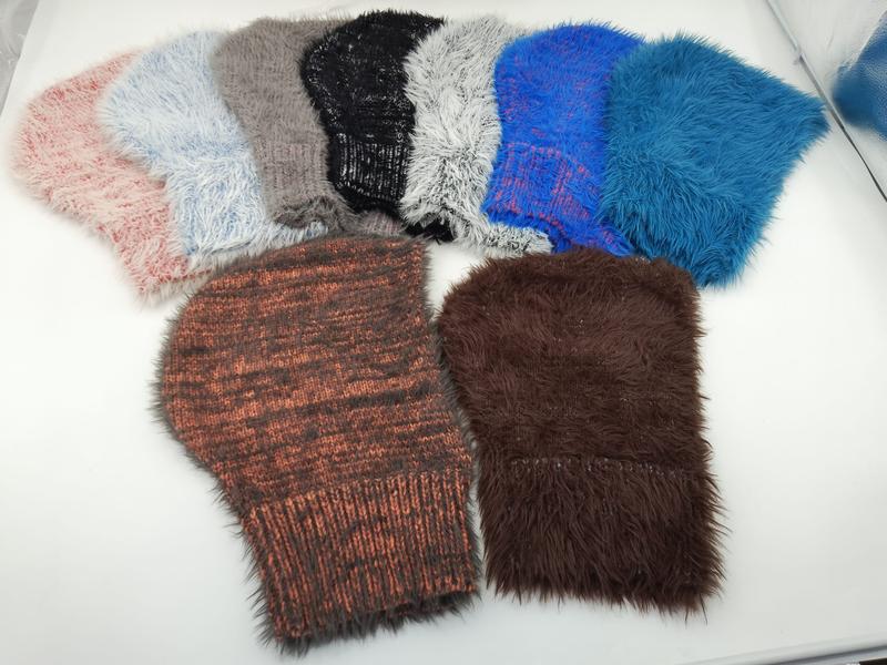 Seven fluffy faux fur and chunky knit beanies in pink, gray, black, white, blue, rust, and brown laid flat on white surface