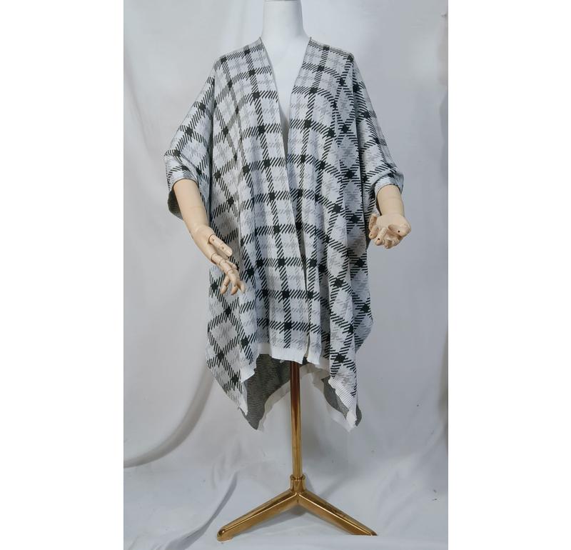 Mannequin wearing a black and white plaid knit open-front poncho wrap cape with draped asymmetric hem on gold stand