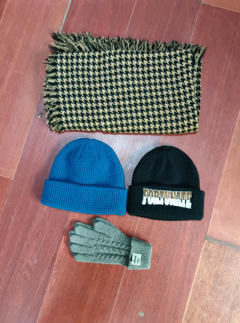 Flat lay of tan black houndstooth fringe scarf, blue waffle knit beanie, black embroidered beanie, and gray cable knit gloves on wood floor