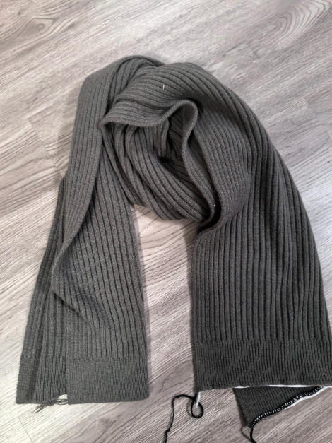 Olive green ribbed knit scarf laid flat on light wood floor, showing full length and texture