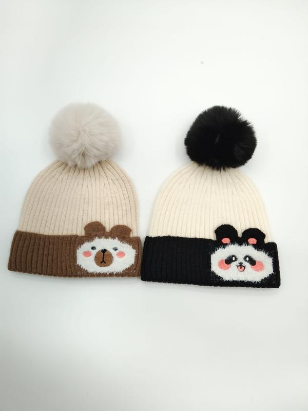 Two knit beanies with pom poms: brown bear design on tan hat and panda design on black and cream hat